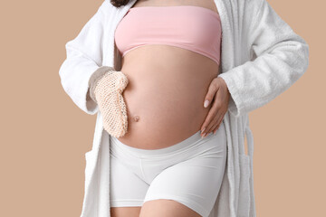 Beautiful young pregnant woman with massage mitten on beige background, closeup