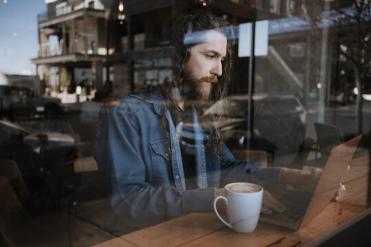 Man working on laptop in coffee shop with street reflection