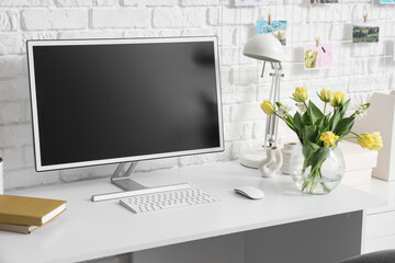 Blank computer monitor and vase with flowers on desk in office