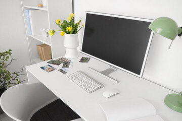 Vase with flowers and blank computer monitor on desk in light office