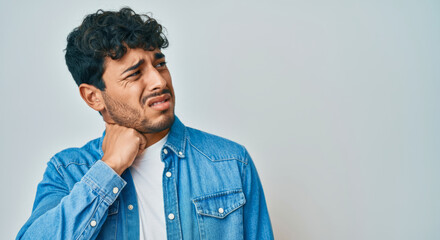 Obraz premium Young hispanic male with neck pain wearing denim jacket against blue background