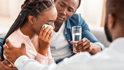Counselor Comforting Desperate Black Woman Crying Next To Husband At Marriage Therapy Session, Young Woman Having Emotional Breakdown Due To Relationship Crisis, Her Spouse Offering Glass Of Water