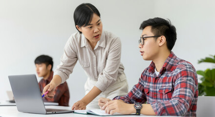 Obraz premium Asian female instructor assisting young male student in classroom with laptop