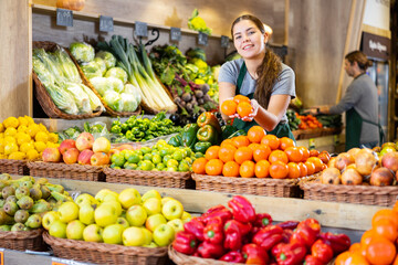 Young woman in apron sells juicy tangerines in greengrocer shop