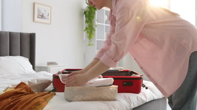 Woman putting clothes into packing cube before placing it in suitcase indoors