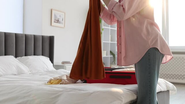 Woman packing skirt into drawstring bag before putting it in suitcase indoors