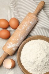 Rolling pin, flour and eggs on light grey background, flat lay