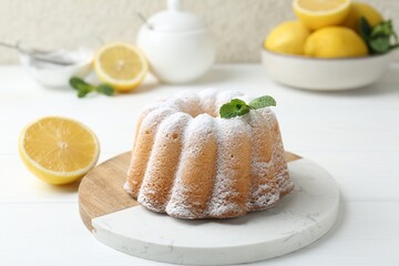 Delicious lemon cake with powdered sugar, mint and citrus fruits on white wooden table, closeup