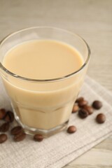 Coffee cream liqueur in glass and beans on table, closeup