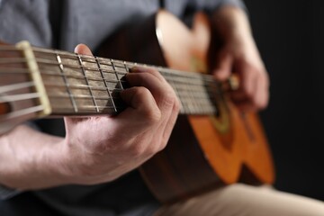 Obraz premium Man playing guitar on black background, focus on hand