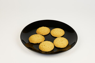 A plate of cookies sits on a white background. The cookies are all the same size and are arranged in a neat row. The plate is black and the cookies are golden brown. Concept of warmth and comfort