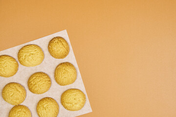 A plate of freshly baked cookies sits on a light brown background. The cookies are small and round, all the same color. The plate is made of aluminum, and the cookies are arranged in rows.
