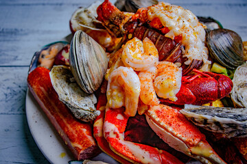 steamed seafood mix in a white plate served with variety of seafood like shells, clams and crab legs.