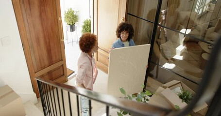 Happy lesbian diverse couple embracing in new home entryway surrounded by moving boxes - Powered by Adobe