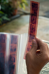Southeast Asian middle-aged man holding undeveloped negative film strips, checking in outdoor...