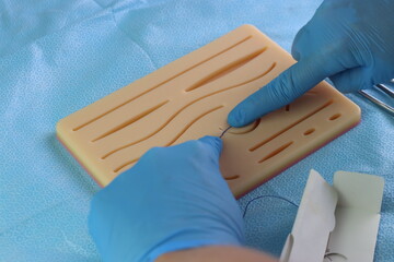 Healthcare professional wearing gloves training surgical suture with a needle in a wound simulation set. Close up in the surgical needle