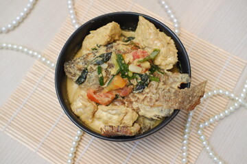 The dish appears to be a rich and creamy coconut milk based curry, featuring a whole fried fish as the centerpiece