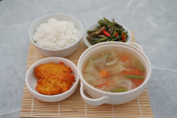 The set includes a bowl of clear vegetable soup filled with cabbage, carrots, and green beans, served in a white bowl with handles