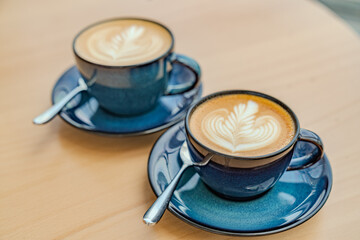Photo of two blue cappuccino coffee cups with a spoon on a wooden table