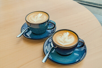 Photo of two blue cappuccino coffee cups with a spoon on a wooden table