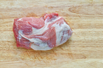 A large piece of raw hip pork and uncut meat tenderloin is on a wooden cutting board. Flat-lay a fresh pork chunk.