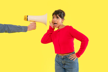 Person reacting to loud announcement while another holds a megaphone against a bright yellow...