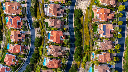 Detailed top-down aerial view of curved residential roads lined with Mediterranean-style homes featuring terracotta roofs and backyard swimming pools in Newport Beach, California. The planned suburban
