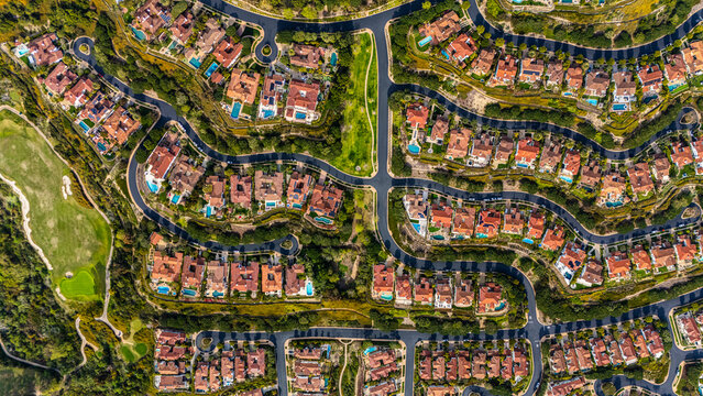 High-resolution aerial photograph showing a planned neighborhood with curved streets and luxury homes with red tile roofs and backyard swimming pools in Newport Beach, California. The community is sur