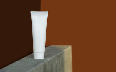 Mockup of white plastic cream tube on rectangular podium made of concrete in rays of sunlight. Container for professional cosmetics. Concept of skin care. Close-up, brown background