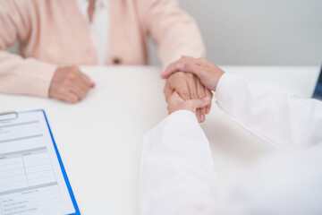 doctor holding hands with elderly female patient, showing empathy and support during a medical...