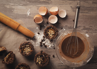 Dark brown muffins, eggshell, rolling pin, glass bowl with dough with cocoa powder, whisk and...