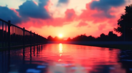 Obraz premium Vibrant colors fill the sky as the sun sets, casting reflections on a serene pathway lined with trees on a peaceful evening