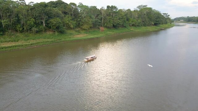 Drone orbit of boat crossing river in Pacaya Samiria National Reserve, Loreto Peru, surrounded by trees and forest