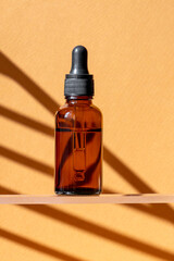 Skincare with beauty cosmetic face serum. Glass bottle amber color with a pipette on brown background with geometric shadow. Dry skin care product. Essential oil for moisturizing body skin.