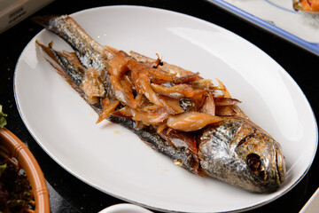Grilled fish on a white plate with fish fillets spread on it
