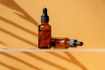 Two Unbranded bottles with pipette on glass shelf. Transparent container made of amber glass with oil for body and hair. Display sample on on a brown background in the sunlight. Mockup style design.