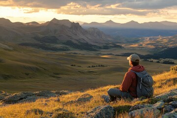 Fototapeta premium Male hiker sitting on a scenic mountain overlooking a vast valley during a golden sunset