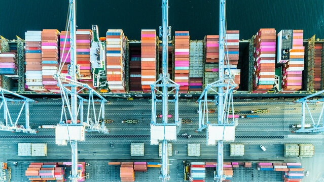 Direct aerial view of a cargo ship docked at a port, with towering cranes loading and unloading colorful shipping containers. A vivid depiction of maritime logistics in action.