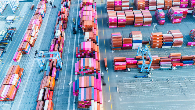 Aerial top view of organized stacks of colorful shipping containers at a busy cargo yard. The image reflects the logistics efficiency and volume of global trade through maritime transport.