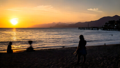 Silhouette of people by the Seaside at Sunset with a Pier in the Distance