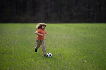 Obraz premium Child playing football in park. Child kicking a football ball on the field. Child running with a football ball. Children playing soccer. Child play football on grass. Summer kids sport. Soccer game.