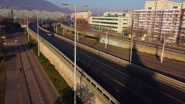 Aerial flyover of busy Budapest highway and bridge as sun sets behind city skyline and river