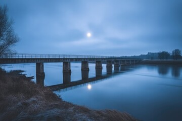 Obraz premium Serene moonlit scene featuring a long bridge spanning a tranquil river under a twilight sky.