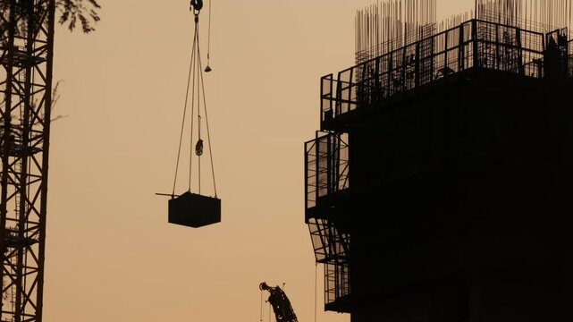 Workers in safety gear supervises the lifting of a container with materials on the building construction site.