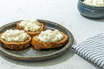 fresh cottage cheese bread slices in rustic blue ceramic plate, striped napkin, bowl with cheese in background on white stone marble table, copy space