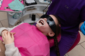 Child undergoing dental treatment in a modern clinic, smiling with excitement while wearing...