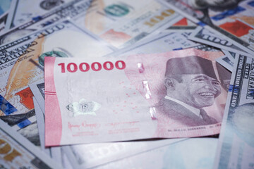 background of piles of US dollar banknotes overlapping Indonesian rupiah banknotes. illustration of inflation of the US dollar currency against the Indonesian rupiah currency
