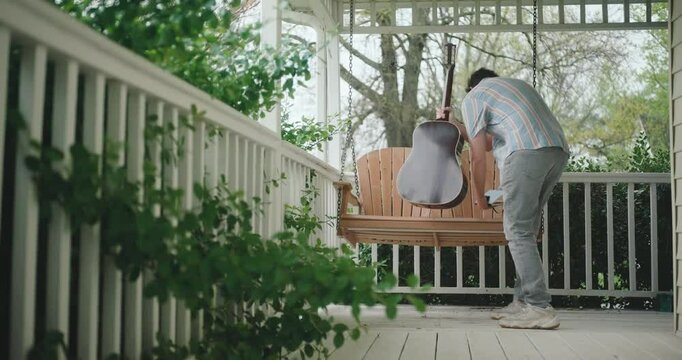 Young male musician sitting on a porch, playing guitar and writing a song