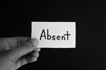 Hand holding a paper card with the word ABSENT