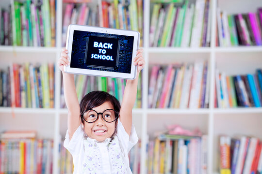 Happy Child Holding Tablet with 'Back to School' Message in Library